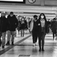 Pessoas andando em um corredor (provavelmente de metrô) usando máscaras contra a pandemia